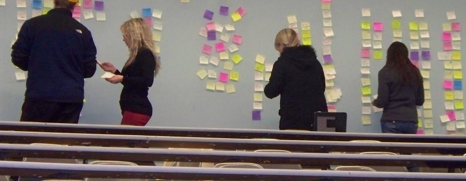 3 females and 1 male are posting post-its on a wall in a classroom