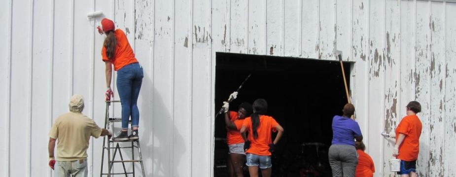 Seven people are painting a barn white