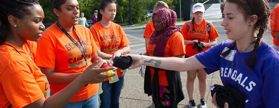 Bengals Dare to Care student leader handing a pair of gloves to female volunteers.  